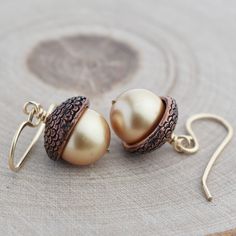 Our gold acorn earrings are perfect for Autumn and Thanksgiving!  The fall earrings are woodland inspired and handcrafted.   Two beautiful gold crystal pearls topped with acorn caps dangle from 14k gold filled earrings.  Whether you're picking apples, enjoying a hayride or Thanksgiving dinner, these nature earrings are festive and fun!  Made with high quality materials they have a bohemian flair and are designed for everyday wear. READY TO GIFT: The jewelry arrives wrapped for easy gifting and includes a jewelry care package.  Add a custom note at checkout that will be printed on a gift card and included with your gift. FIT: 1 ¼  inches long MATERIALS *Crystal pearls - Highly resistant to UV rays and perfumes, ideal for long-lasting jewelry. *Acorn caps - Copper-plated pewter, designed in Acorn Jewelry, Acorn Earrings, Woodland Earrings, Earrings Fall, Nature Earrings, Open Hoop Earrings, Fall Earrings, Nature Inspired Jewelry, Gold Filled Earrings