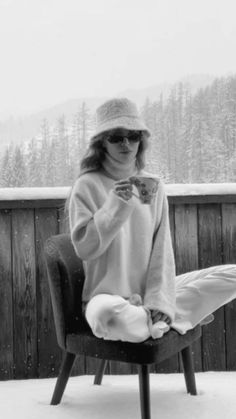 a woman sitting in a chair on top of a snow covered ground holding a cup