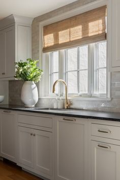 a kitchen with white cabinets and black counter tops has a vase on the window sill