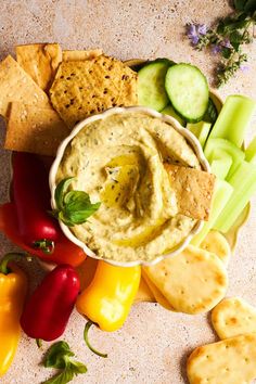 an assortment of vegetables and crackers on a table with dip in a bowl next to them