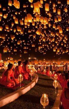 many people are sitting on the ground with lanterns floating in the air