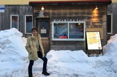 a woman standing in front of a building with snow piled on the ground and around her