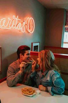 a man and woman sitting at a table in front of a neon sign that reads, la ceriata's