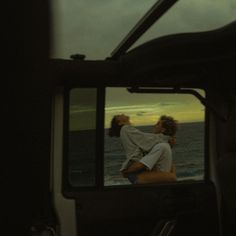 two women are kissing in the rear view mirror of a vehicle near the ocean at sunset