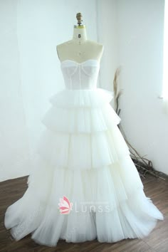 a white wedding dress with tiered layers on the skirt and bustle is displayed in front of a mannequin