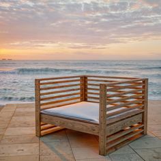 a wooden bench sitting on top of a stone floor next to the ocean at sunset