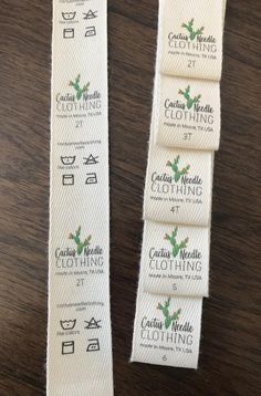 three white cotton clothing labels on a wooden table, one with green leaves and the other has