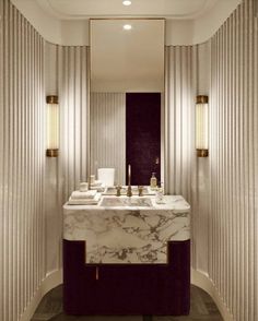 a bathroom with marble counter top and gold trim around the sink, along with wall sconces