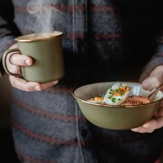 a person holding a bowl with food in it and two cups next to each other