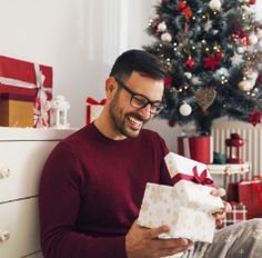 a man sitting in front of a christmas tree holding a present