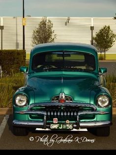 an old green car parked in a parking lot