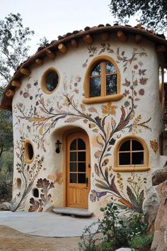 an unusual house made out of stucco with windows and flowers painted on the outside wall