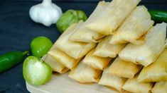 several pieces of tamales on a cutting board next to peppers and green bell peppers