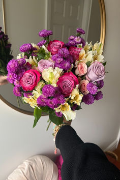 a person holding a bouquet of flowers in front of a mirror with their hand on it