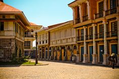 an empty street with old buildings and people walking around the building on either side,