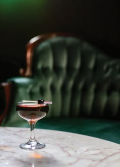 a table with a wine glass on it and a green velvet chair in the background