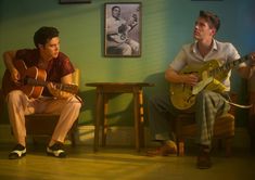 two young men sitting in chairs playing guitars and one is holding a guitar while the other sits on a chair