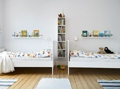 two white beds in a room with bookshelves and rugs on the floor