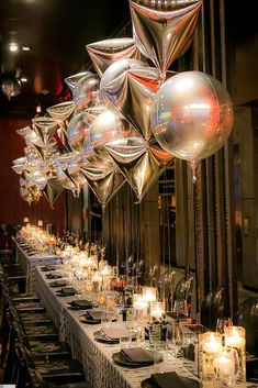 balloons and candles are hanging from the ceiling in front of a long table with white linens