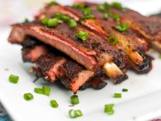 a white plate topped with ribs covered in sauce and green onions