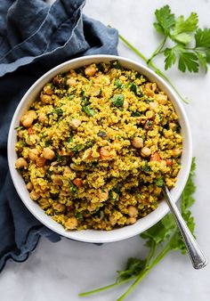 a white bowl filled with rice and vegetables on top of a blue napkin next to cilantro