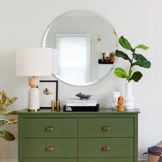 a green dresser with a round mirror above it and a lamp on top of it