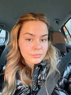 a woman sitting in the back seat of a car wearing a black jacket and looking at the camera