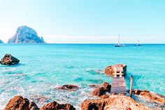 a chair sitting on top of a rocky beach next to the ocean with boats in the water