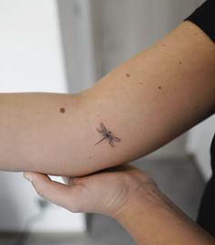 a woman's arm with a small dragonfly tattoo on the left side of her arm