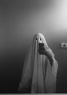 a person in a ghost costume taking a photo with a cell phone on the wall