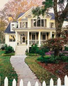 a white house with lots of trees and flowers in front of the porch, stairs leading up to the second floor