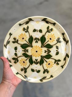 a hand holding a yellow and white plate with flowers on it's side,