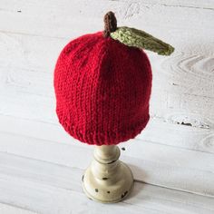 a red knitted hat sitting on top of a white wooden stand with a green leaf sticking out of it