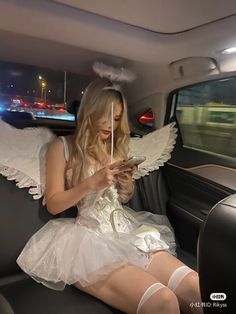 a woman sitting in the back seat of a car looking at her cell phone with angel wings on it