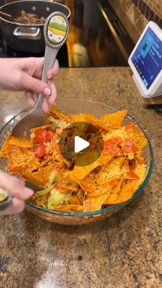 two hands are scooping tortilla chips into a glass bowl on the counter