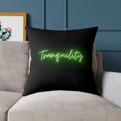 a black pillow with the word tranquility in neon green on it next to a couch