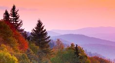 the sun is setting in the mountains with trees on each side and colorful foliage below