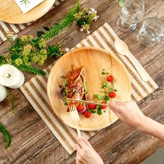 a person holding a fork over a wooden plate with food on it and greenery