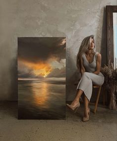 a woman sitting on a chair in front of an art piece with the sun setting