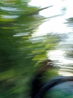 blurry image of a man riding a skateboard down a hill with trees in the background