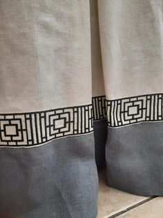 two gray curtains with black and white designs on the top one is open, while the other is closed