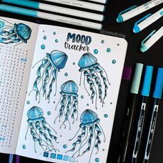 an open notebook with blue markers and some jellyfishs on the pages, next to pens