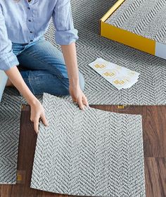 a woman is sitting on the floor with her feet up and cutting out carpet tiles