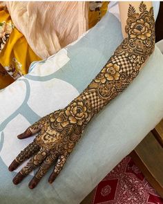 a woman's hand with henna tattoos on her arm and hands, sitting on a chair