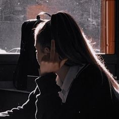 a woman sitting in front of a window with her hand on her face while talking on the phone