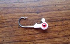 a fishing hook with a red eye on it sitting on a wooden table next to a pair of scissors