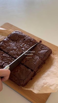 a person cutting into brownies on top of a wooden cutting board with a knife