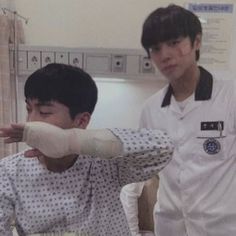 two young men standing next to each other in front of a hospital room with an arm cast on his head