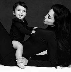 a woman holding a baby while sitting on top of her lap and posing for a black and white photo