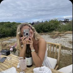 a woman sitting at a table taking a photo with her cell phone while holding a wine bottle